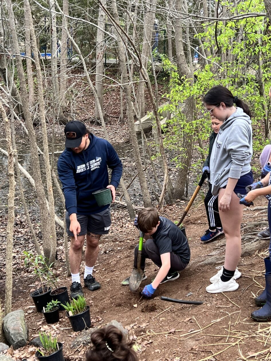 A preservice teacher helps students plant in a forest.