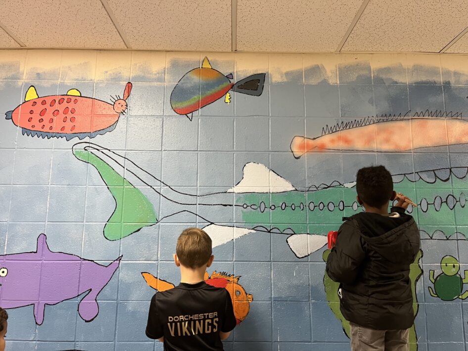 Two students paint a colorful mural of endangered fish on the wall of their elementary school.