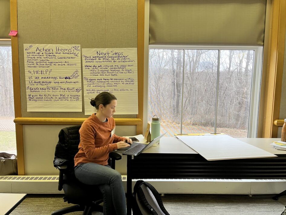 One educator takes notes on a computer in a conference room decorated with hanging note papers from a previous collaboration session.