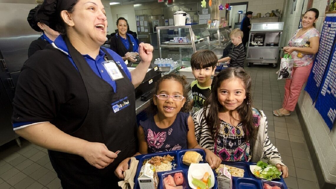 Children proudly show their lunch trays filled with fruit and vegetables.