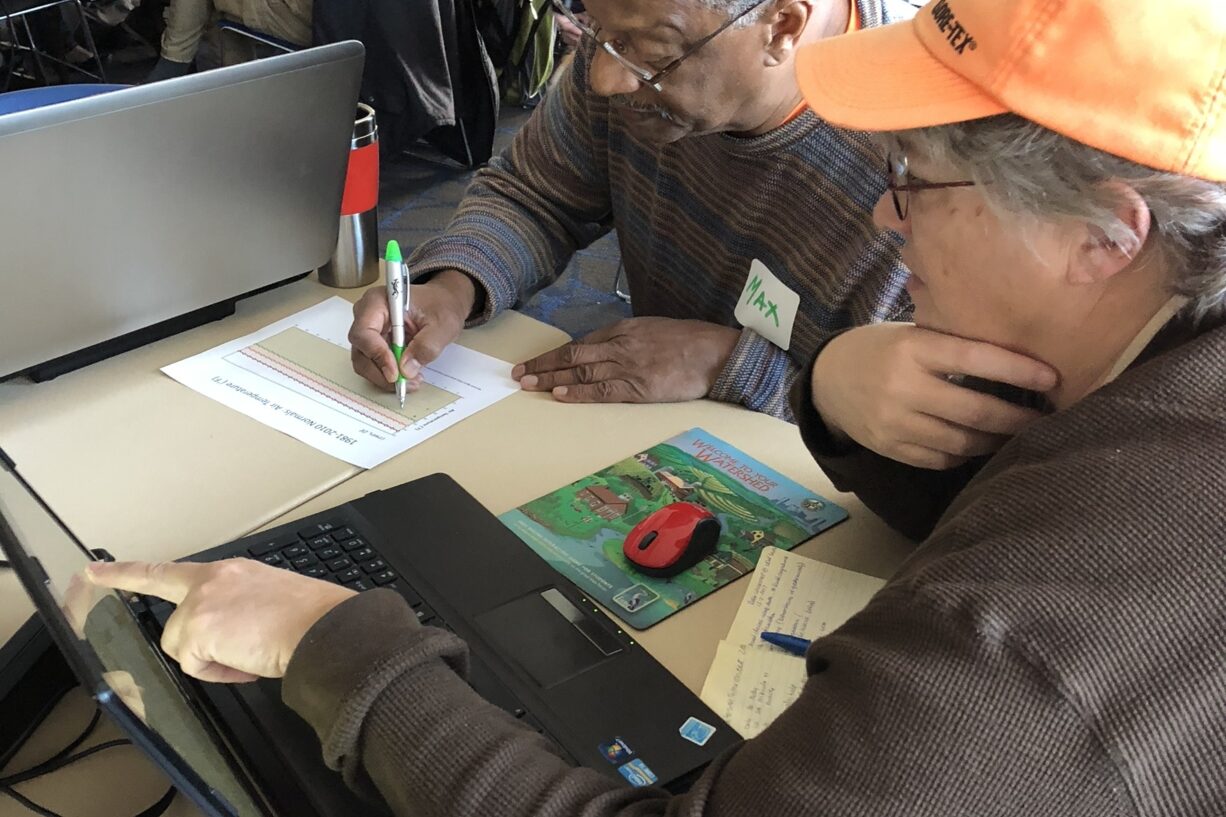 A woman points to a laptop screen while her partner takes notes.