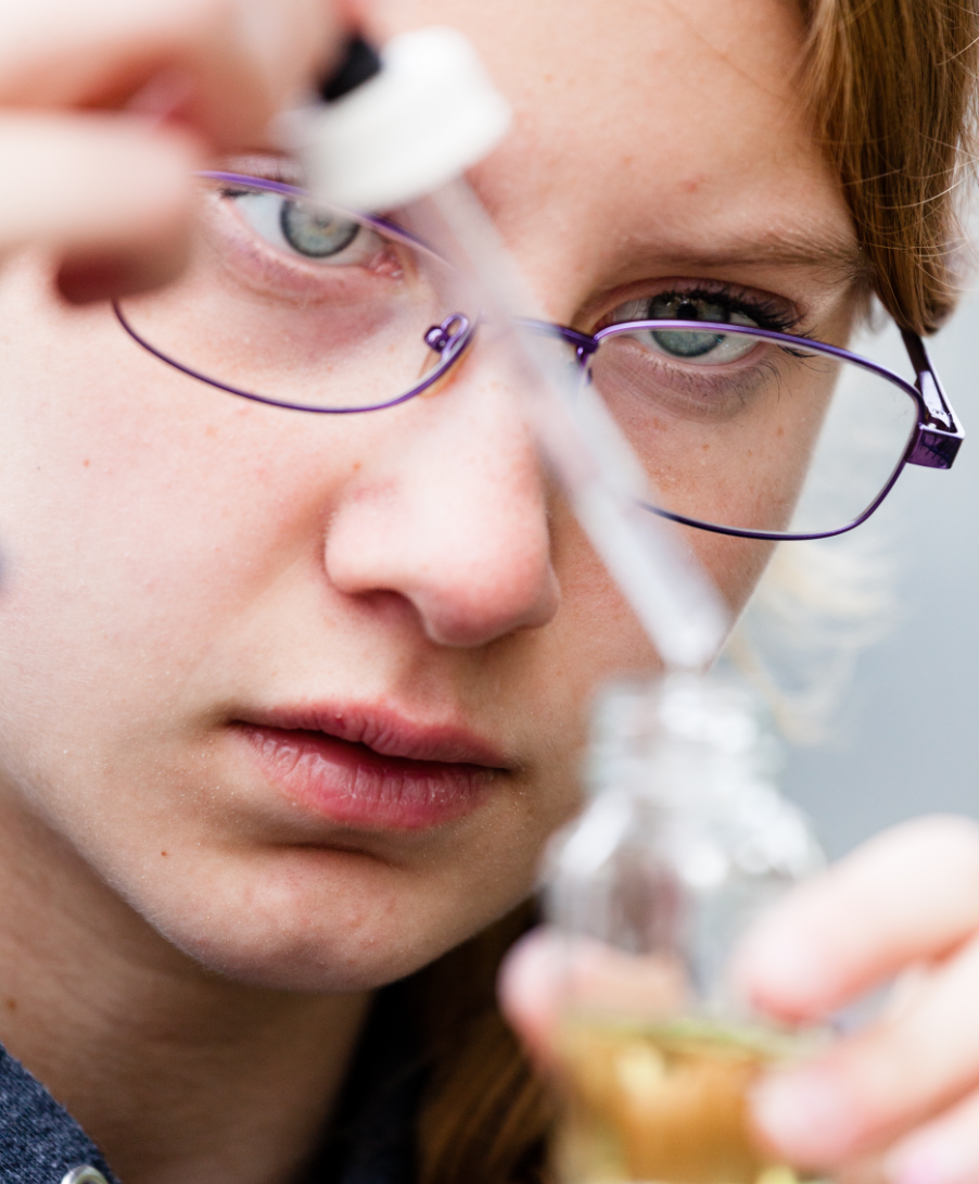 Young student carefully uses a dropper to take a sample from a beaker of dirty water.