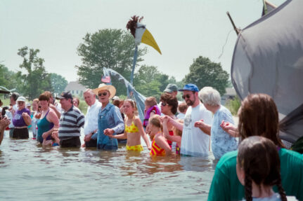 Group of people hold hands while standing waist deep in the water.