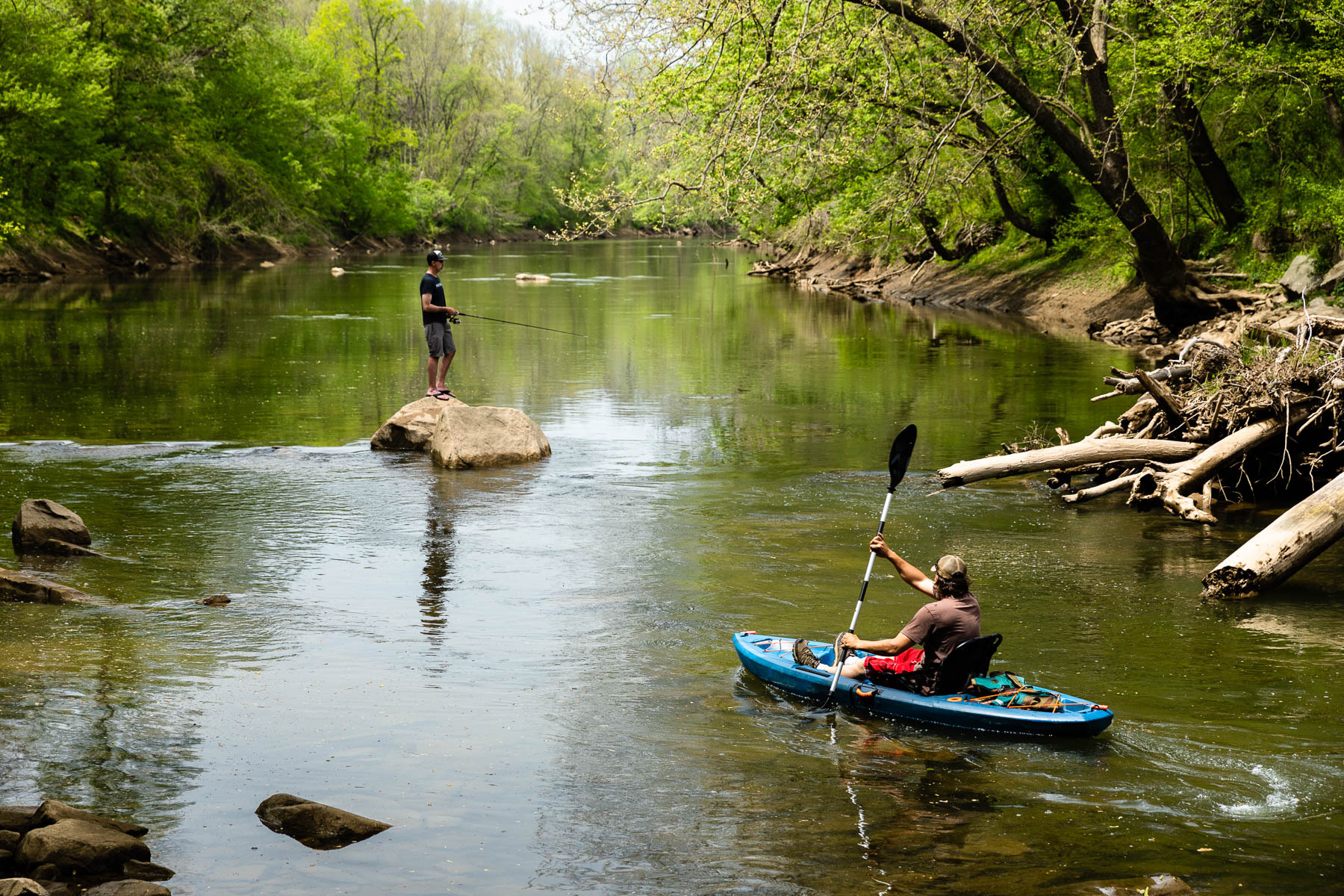 Two kayakers paddle down a forested river